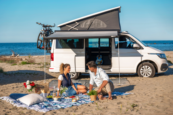 Weißer VW BUs am Strand mit Markise und Decke und Familie davor